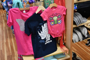 photo - variety of baby/childrens onsies, t-shirts, adult shirts, you can purchase at zoo gift shop, with view of ballcaps also available to buy