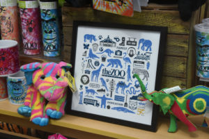 photo - 50th anniversary gifts you can purchase at gift shop - coffee cups, plush animals, water canisters, print of zoo animals, signs, playground, family, camera, others in black, blue shadow images in a black frame