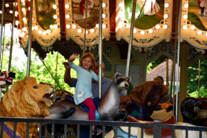 photo - smiling little girl on carousel animal ferret, waving to visitors