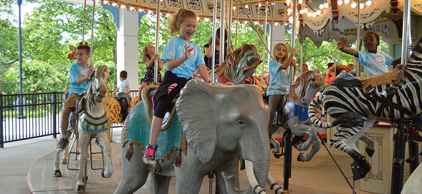 photo - variety of children on carousel animals, horse, elephant, zebra, tiger, all smiling, laughing, having fun