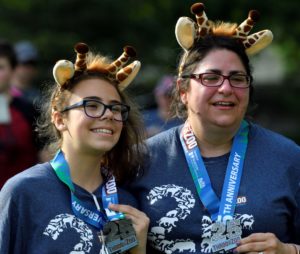 photo - two female ThrootheZoo participants, wearing giraffe ears headbands, wearing 25 anniversary, Throo the Zoo, lanyards with 25th anniversary medals hanging on them, wearing t shirts, for 25th anniversary run/walk