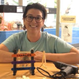 photo by mckenzie - employee sitting in meta zoo, at table with materials needed and finished product of earring holder made for kids arts and crafts session