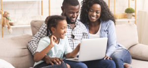 photo - family, mom, dad, child, sitting on couch, laughing, smiling, as they use laptop for entertainment