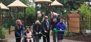 photo - accessible playground dedication, 5 adults, 1 child in wheelchair, cutting ribbon to open accessible playground