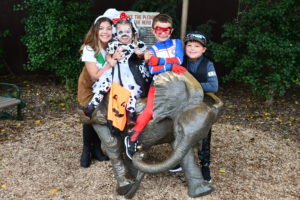 photo of 4 children, in halloween costumes sitting on the fitz memorial statue, background is green bushes