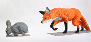 graphic - Lego sculptures of grey rabbit with white paws and white fluff puff tail with Lego sculpture of orange fox with black forelegs and paws, black ears with white trim, white chest fur, long orange tail, following rabbit
