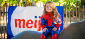 banner of child in Spiderman outfit, on rhino statue, at rhino yard, with meijer banner in background