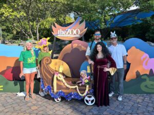 photo of family dressed in halloween costumes, in front of zoo animal plaza display, with small child sitting in stroller made into a boat